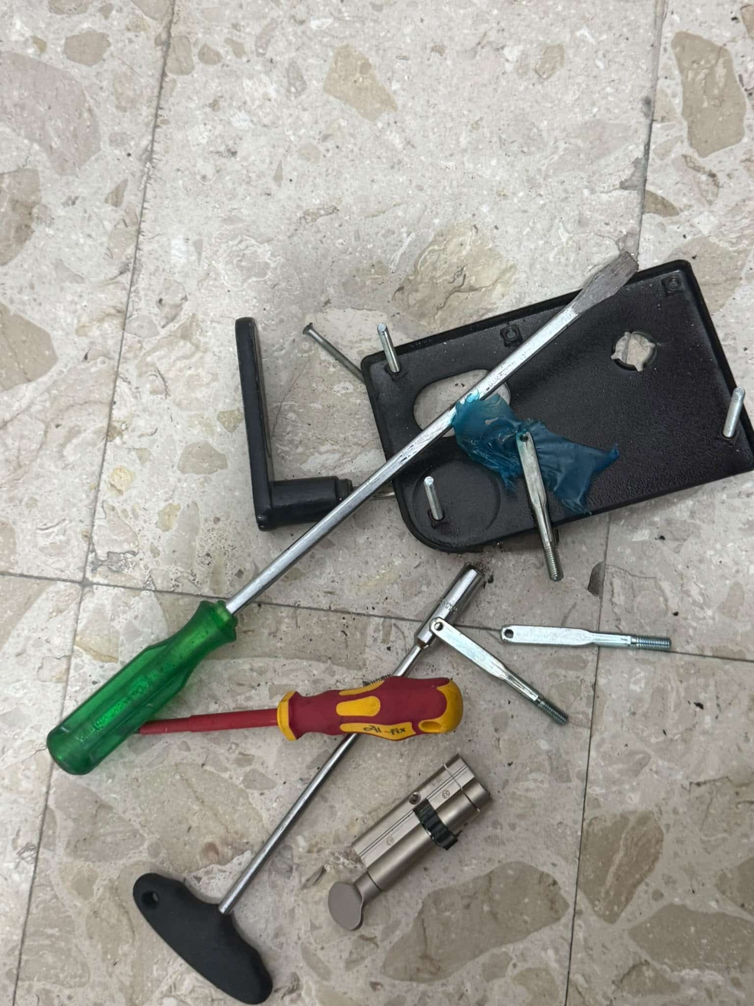 פלטת הידית השחורה שפורקה מהדלת, לצד הצילינדר החדש והכלים