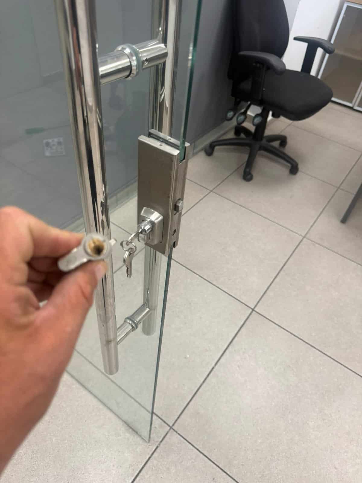 צילינדר חדש עם מפתחות במנעול דלת הזכוכית, והצילינדר הישן ביד