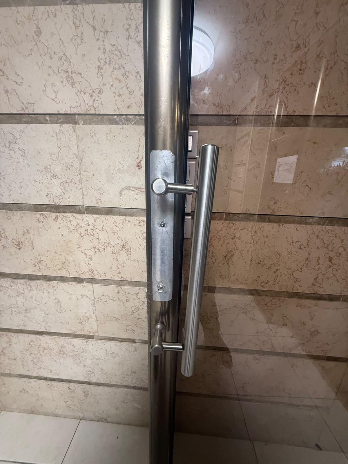 דלת הכניסה לבניין ברמת גן אחרי התיקון, עם לוחית נירוסטה חדשה, כפתור וידית משיכה ארוכה